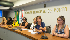 Vereadora Nádia, ao microfone, vereadora Mônica e convidadas na mesa principal do evento