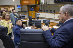 Movimentação de plenário. Em primeiro plano os vereadores Giovani Culau e Coletivo, Biga Pereira e Idenir Cecchin. Ao fundo, na tribuna, o vereador Jessé Sangalli.